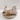 Colostrum soap bar next to another bar in packaging on a brown platter with a tan vase that has brown fauna in it