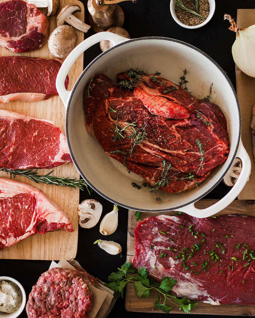Raw steaks on a cutting board with seasonings and ingredients on a dark surface